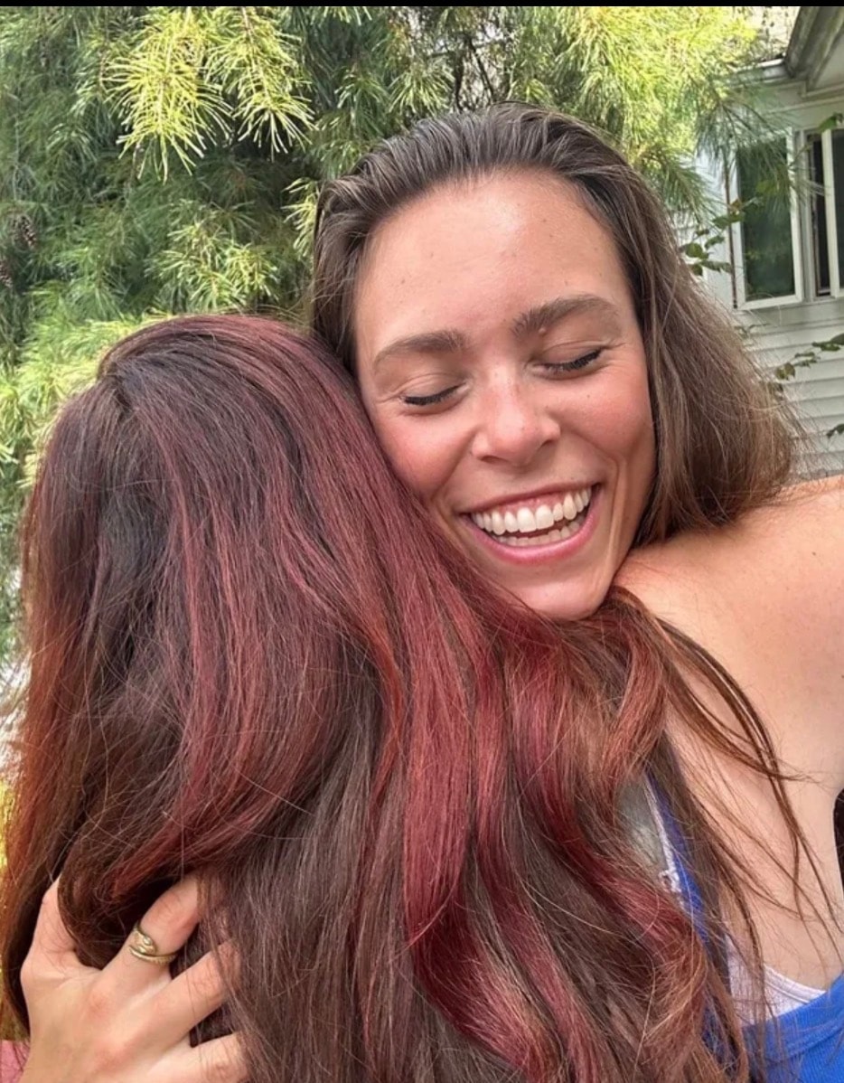 Angela smiling joyfully while hugging someone outdoors