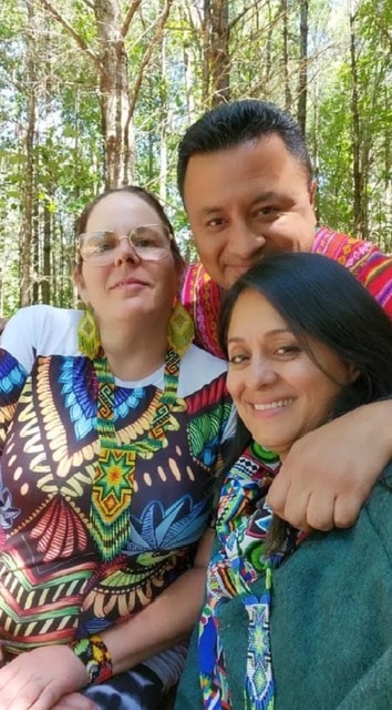 Three people smiling together in a lush forest setting