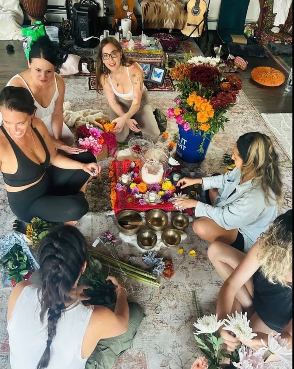 Women sitting in circle with flowers and singing bowls during a ceremony