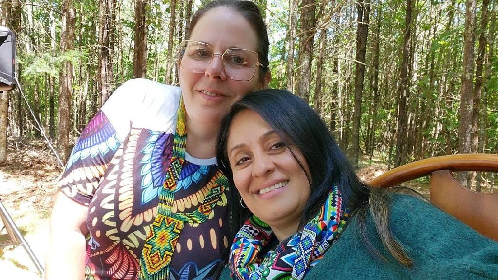Angela smiling with a friend in a sunny forest setting