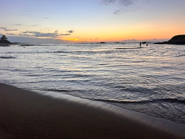 Peaceful beach sunset with gentle waves and silhouetted figures in the water