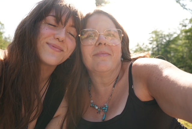 Angela and a friend smiling together in warm sunlight outdoors