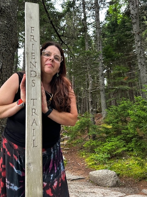 Angela leaning against a Friends Trail sign in the forest